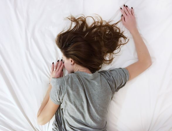 femme allongée en t-shirt dans un lit sur le ventre les bras en l'air
